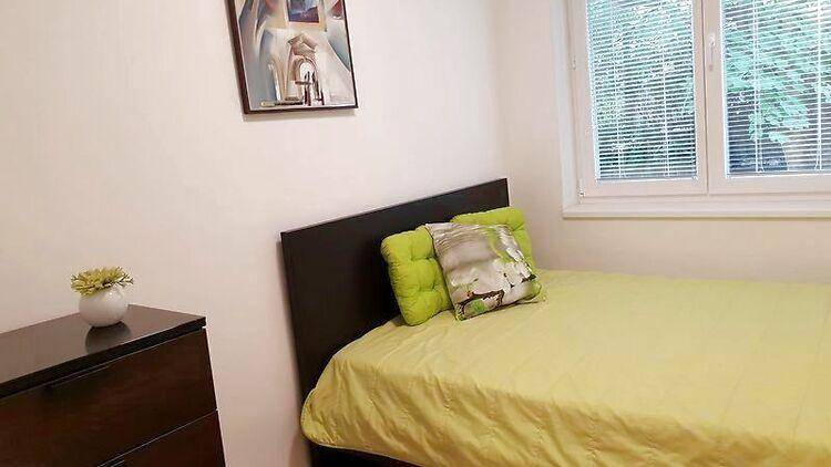 Helles Schlafzimmer mit Einzelbett, dunkler Kommode und Fenster mit Blick ins Grüne.