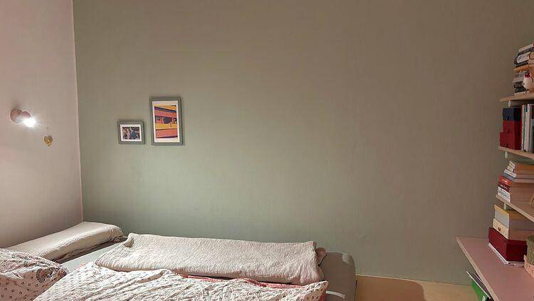 Schlafzimmer mit schlichten grünen Wänden, einem Bett und einem Bücherregal an der Seite.