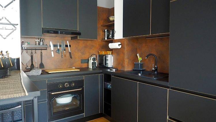 Moderne Küche mit schwarzen Schränken, dunkler Arbeitsplatte und rostfarbener Rückwand.