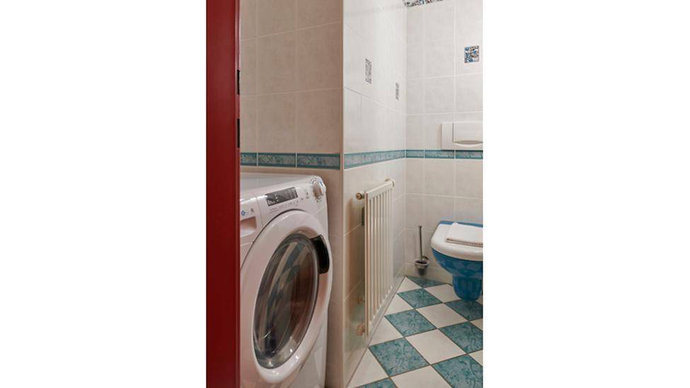 Kleines Badezimmer mit WC, Waschmaschine und farbigen Bodenfliesen.