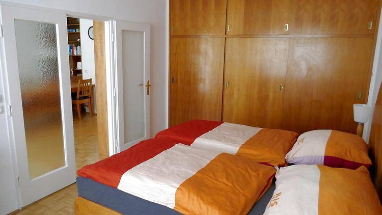 Schlafzimmer mit Doppelbett, Einbauschränken aus Holz und Zugang zum Wohnbereich.