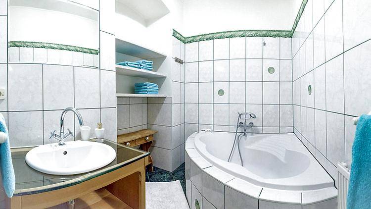 Badezimmer mit Eckbadewanne, Waschbecken und weißen Fliesen mit grünen Akzenten.