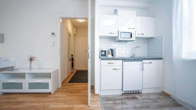 Kompakte Küchenzeile in einem Studio-Apartment mit weißer Einrichtung und Holzboden.