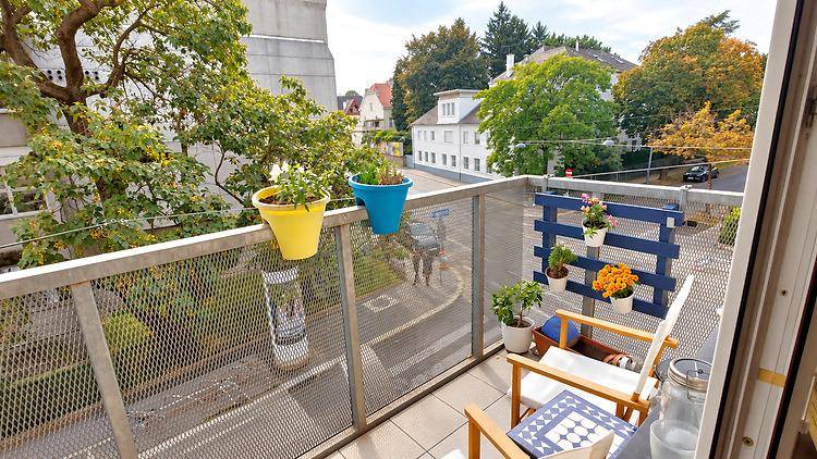 Kleiner Balkon mit Metallgeländer, Pflanzen und Blick auf die umliegende Wohngegend.