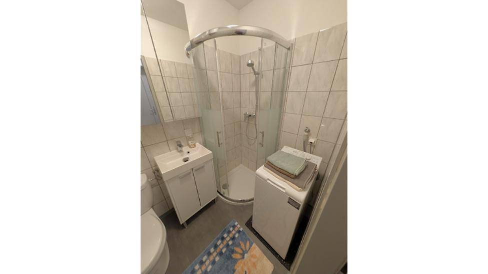 Badezimmer mit Duschkabine, Waschbecken und integrierter Waschmaschine.