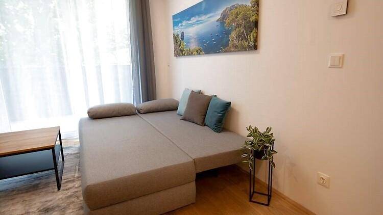 Helles Wohnzimmer mit ausziehbarer Schlafcouch und Blick auf die grüne Umgebung.