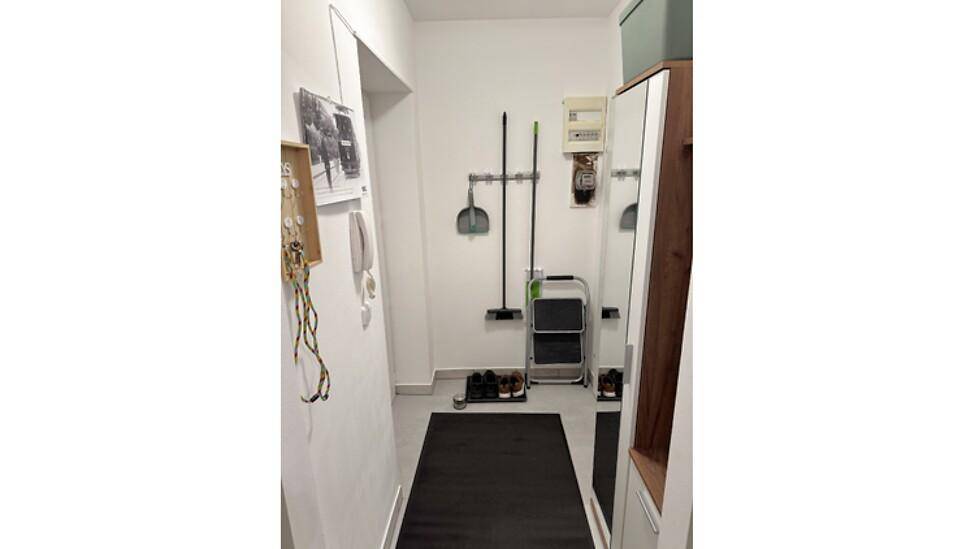Schmaler Flur mit Reinigungsutensilien und einem Stromkasten an der Wand.
