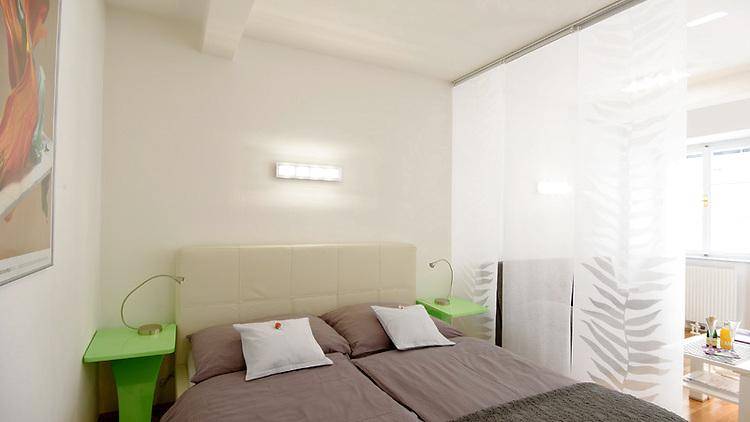 Detailansicht des Schlafbereichs mit Doppelbett, Nachttischen und dekorativem Raumteiler.