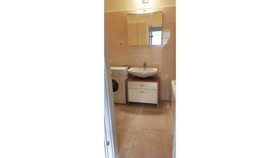 Badezimmer mit Waschbecken, Spiegelschrank und Waschmaschine, hell gefliest.