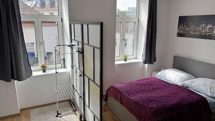 Schlafzimmer mit zwei großen Fenstern, die viel Tageslicht hereinlassen und einen Blick nach draußen bieten.