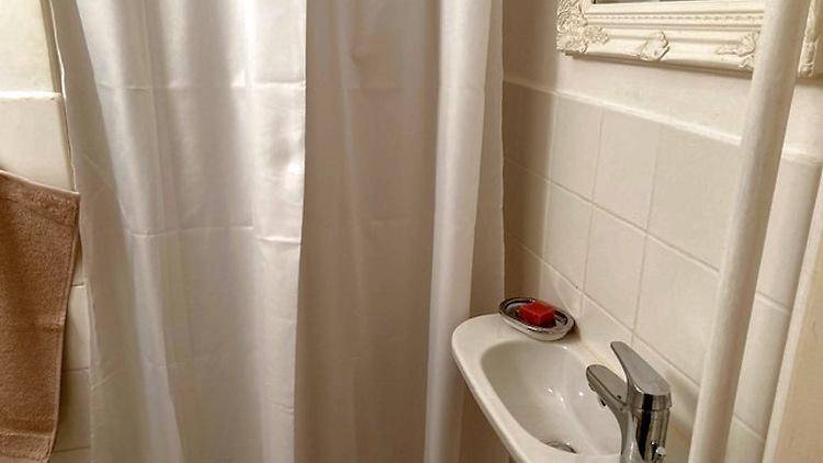 Badezimmer mit Duschvorhang, kleinem Waschbecken und weißen Fliesen.