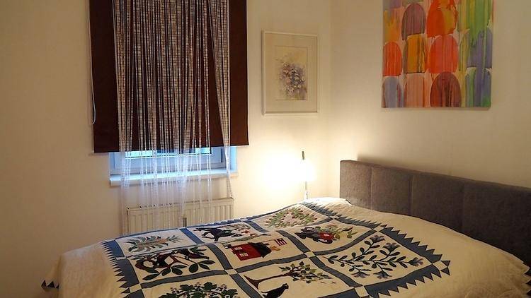 Schlafzimmer mit Doppelbett, gemusterter Tagesdecke und einem Fenster mit Jalousie.