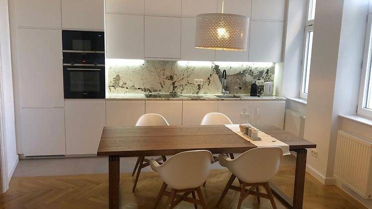 Moderne weiße Küche mit Holztisch und Stühlen, ausgestattet mit Einbaugeräten und Marmor-Rückwand.