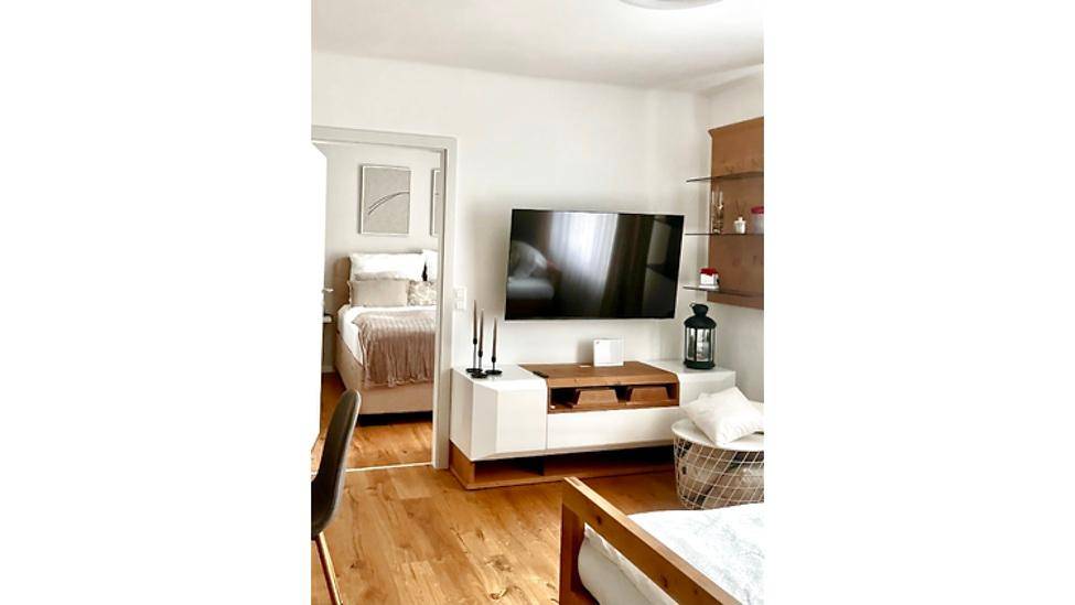 Gemütlicher Wohnbereich mit Fernseher, Medienschrank und Blick in ein angrenzendes Schlafzimmer.