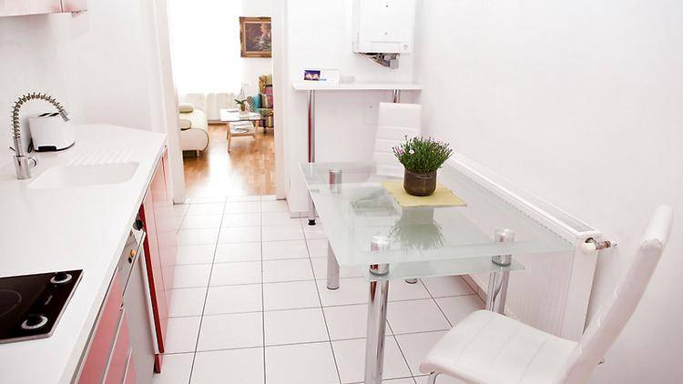 Kleine Küche mit Essbereich, roten Schränken und Fliesenboden, offen zum Wohnzimmer hin.