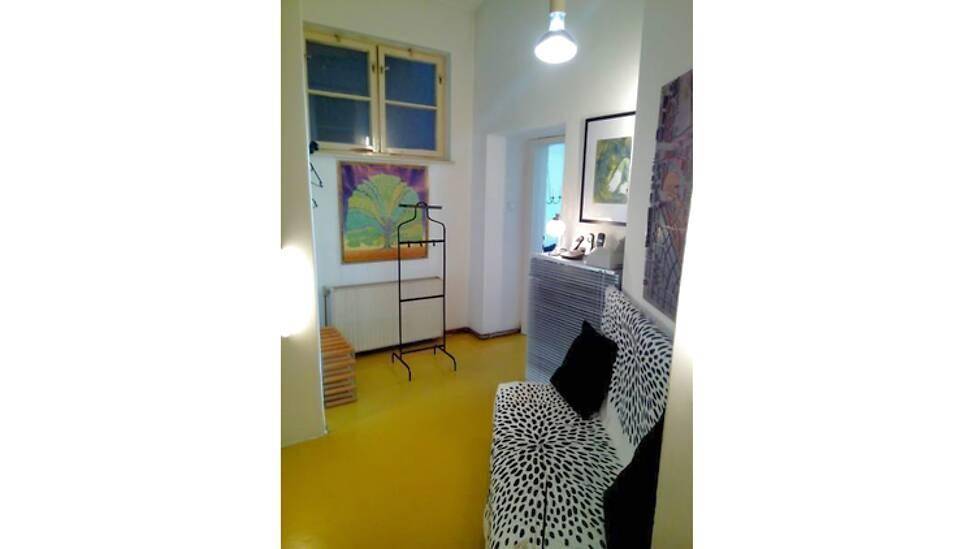 Kleiner Raum mit gelbem Boden, Sofa und Fenster, dekoriert mit Kunstwerken.