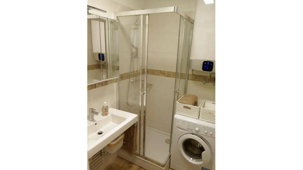 Modernes Badezimmer mit Duschkabine, Waschbecken und integrierter Waschmaschine.