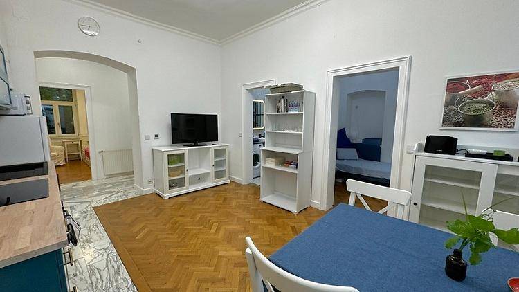 Heller offener Wohn- und Essbereich mit Parkettboden, Fernseher und Zugang zu weiteren Räumen.