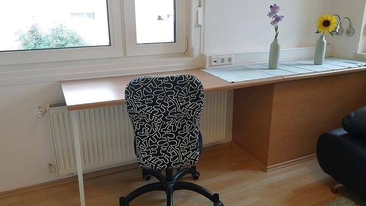 Arbeitsbereich am Fenster mit Schreibtisch, Bürostuhl und Heizkörper.