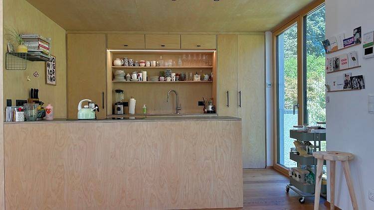 Moderne Küche mit hellen Holzfronten, Kücheninsel und großem Fenster mit Blick ins Grüne.