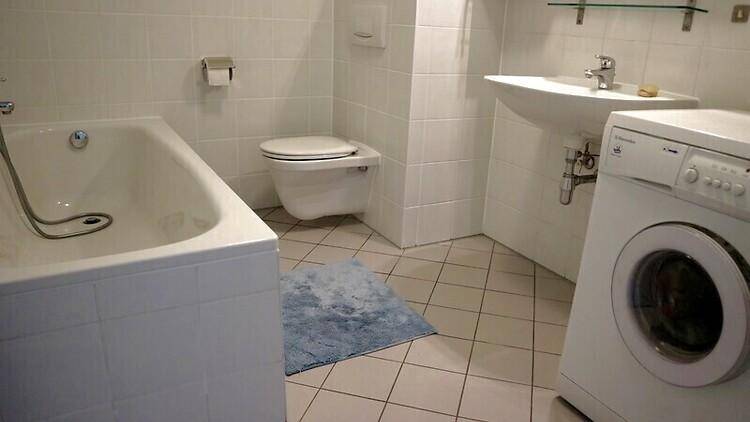 Gefliestes Badezimmer mit Badewanne, wandhängendem WC, Waschbecken und Waschmaschine.