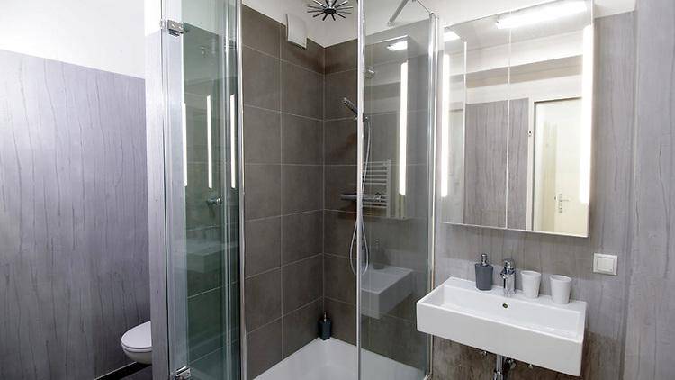 Modernes Badezimmer mit begehbarer Dusche, Einzelwaschbecken und grauen Fliesen.