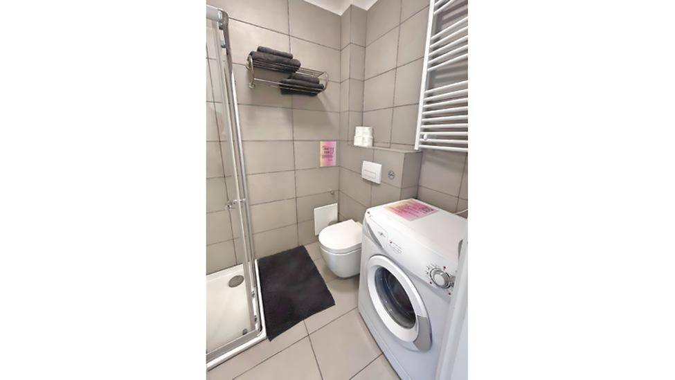 Modernes Badezimmer mit Duschkabine, WC, Waschmaschine und beheiztem Handtuchhalter.