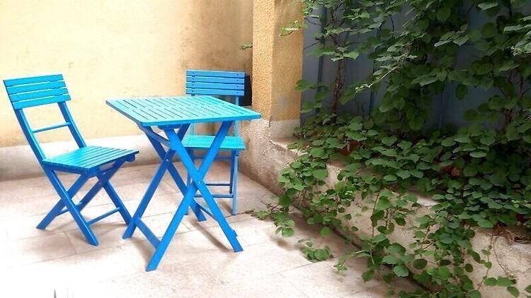 Gemütlicher Außenbereich mit blauen Klappstühlen und Tisch, umgeben von Grünpflanzen, ideal für entspannte Stunden.