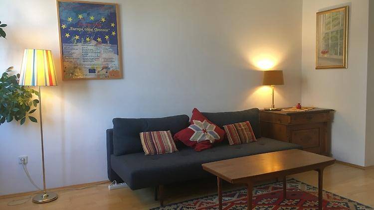 Helles Wohnzimmer mit bequemem Sofa, Stehlampe und einem Teppich mit geometrischem Muster.