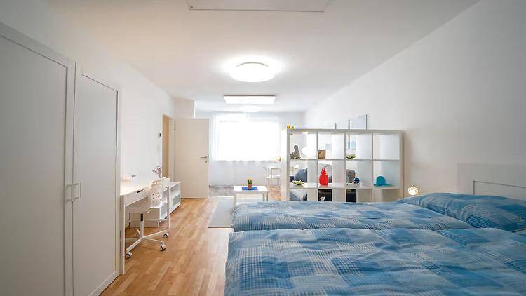 Schlafbereich in einem Studio-Apartment mit zwei Einzelbetten, Schreibtisch und hellem Holzboden.