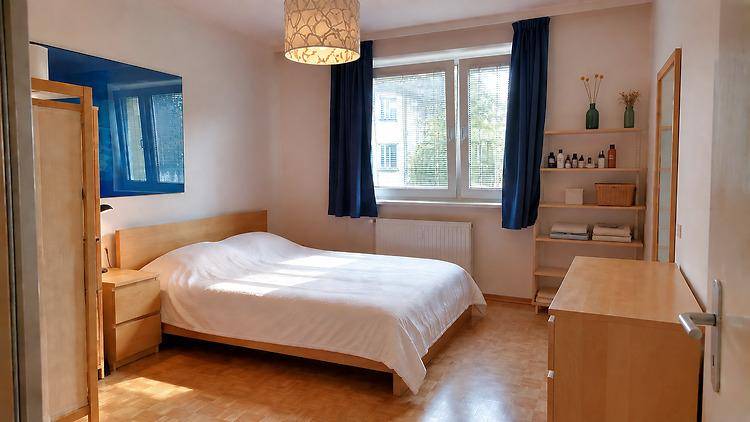Schlafzimmer mit Doppelbett, Holzmöbeln, blauen Vorhängen und Fenster mit Blick ins Grüne.