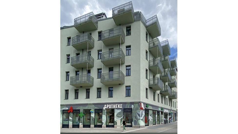 Modernes Mehrfamilienhaus mit zahlreichen Balkonen und einer Apotheke im Erdgeschoss.