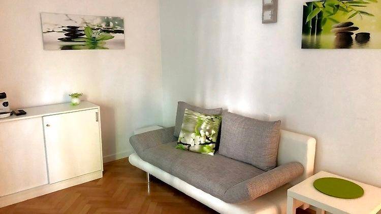 Gemütliches Wohnzimmer mit hellem Parkettboden und einem bequemen Sofa, dekoriert mit grünen Akzenten.