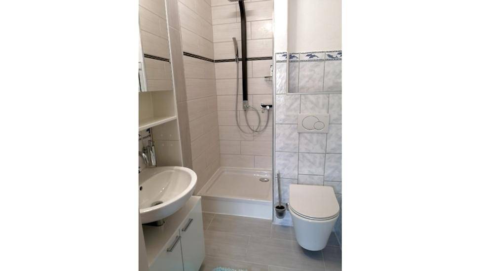 Modernes Badezimmer mit Dusche, Waschbecken und WC, hell gefliest.