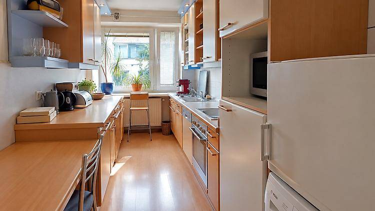 Funktionale Küche mit Holz- und weißen Schränken, Fenster und integrierten Geräten.