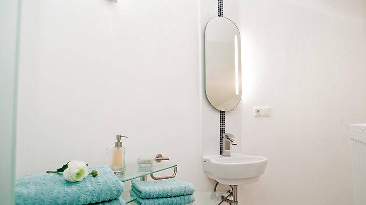 Modernes Badezimmer mit kleinem Waschbecken, beleuchtetem Spiegel und weißen Fliesen, funktional und hell gestaltet.