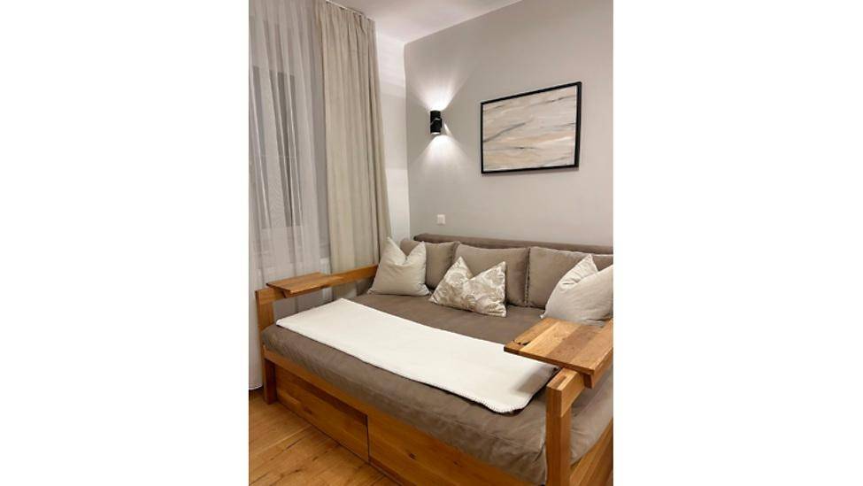 Komfortables Schlafsofa in einem hellen Raum mit Holzboden, Vorhängen und Wanddekoration.