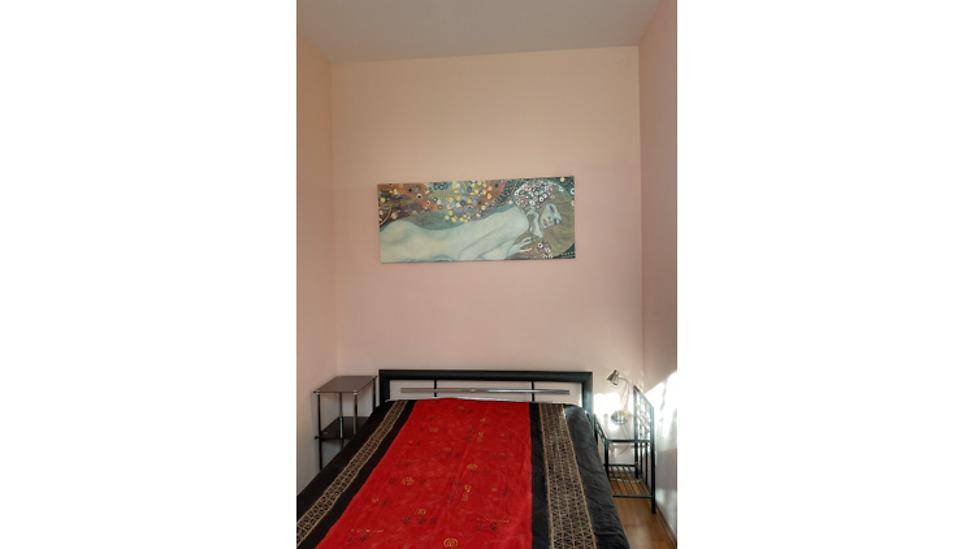 Schlafzimmer mit Doppelbett, Kunstwerk über dem Bett und hellrosa gestrichenen Wänden.