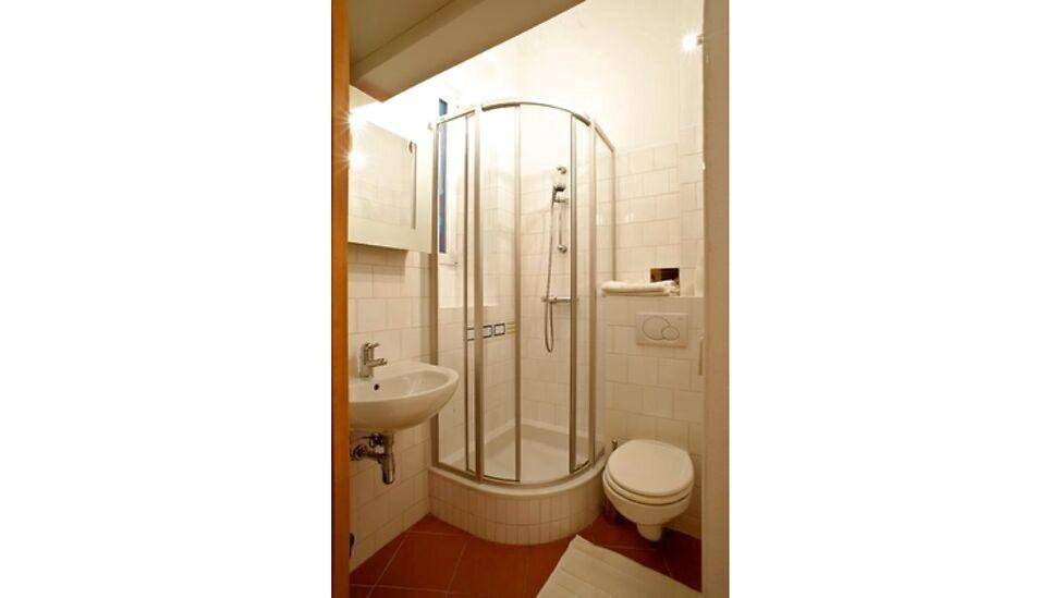 Kleines Badezimmer mit Eckdusche, WC, Waschbecken und terracottafarbenen Fliesen.