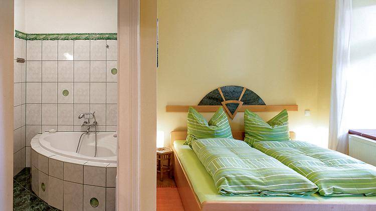 Schlafzimmer mit zwei Einzelbetten und Blick auf ein Badezimmer mit gefliester Eckbadewanne.