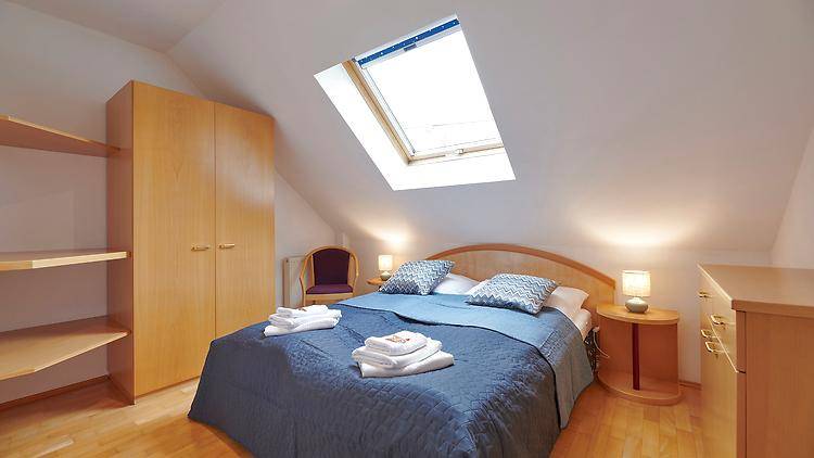 Helles Schlafzimmer mit Dachfenster, Doppelbett und praktischen Holzschränken.