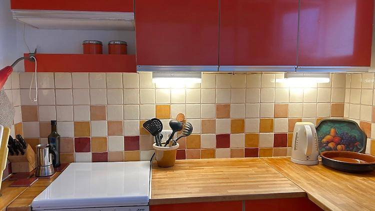 Funktionale Küche mit roten Schränken, Holz-Arbeitsplatte und bunten Fliesen an der Wand.