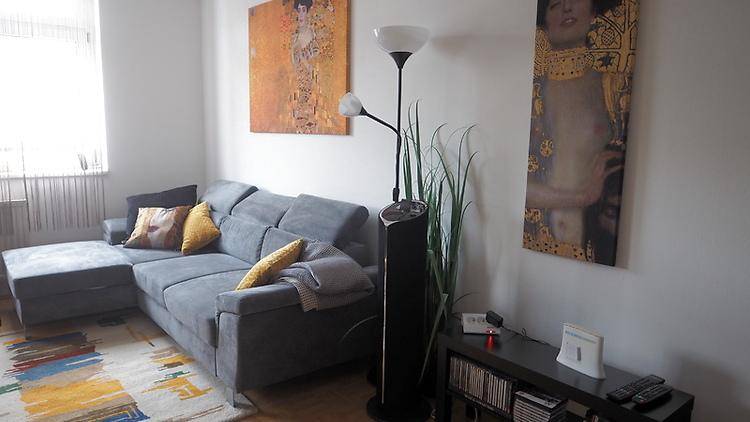 Helles Wohnzimmer mit bequemer Eckcouch, Stehlampe und Kunstwerken an den weißen Wänden.