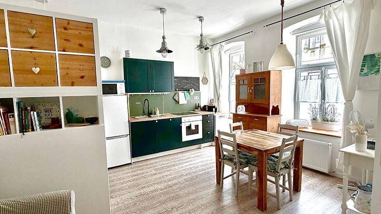 Grüne Einbauküche mit Holztisch und Stühlen in einem hellen Raum mit hohen Decken.