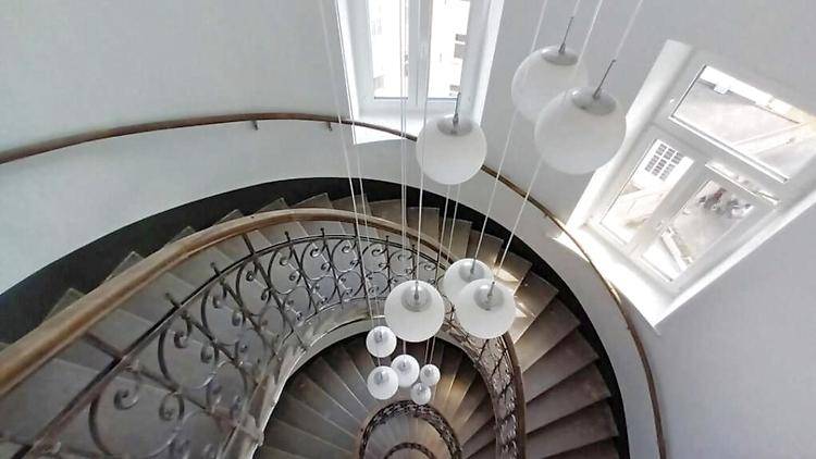 Elegantes Treppenhaus mit geschwungener Wendeltreppe, schmiedeeisernem Geländer und modernen Hängelampen.