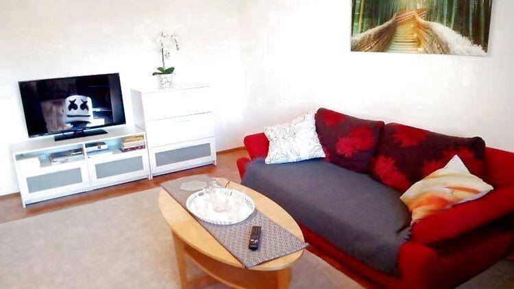 Gemütliches Wohnzimmer mit rotem Sofa, Couchtisch und Fernseher auf einem weißen Sideboard.