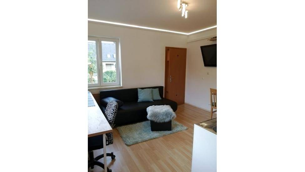 Gesamtaufnahme des hellen Wohnbereichs mit Sofa, Esstisch und integrierter Küchenzeile.