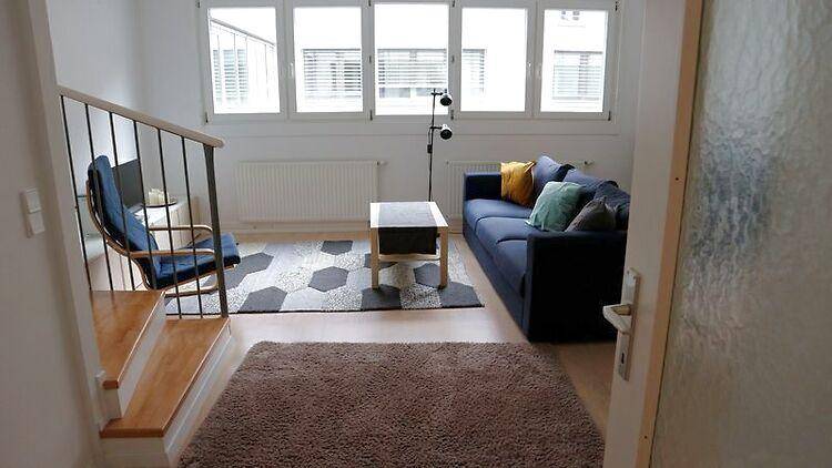 Helles Wohnzimmer mit großen Fenstern, Sofa und Teppichboden, bietet einen grünen Ausblick.