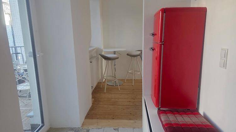 Kleine Küchenzeile mit auffälligem rotem Kühlschrank, Barhockern und Zugang zum Balkon.