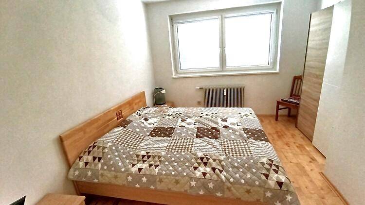 Schlafzimmer mit Doppelbett, Holzbettrahmen und Fenster mit Heizkörper.